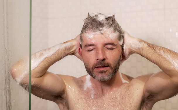 morning shower - lifestyle portrait of young attractive and happy man with beard taking a shower at home washing his hair with shampoo enjoying cheerful in wellness and hygiene concept - Photo, Image
