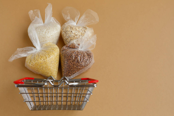 various groats in packages in a grocery basket on a brown background. Rice and oatmeal, buckwheat and millet - Foto, afbeelding