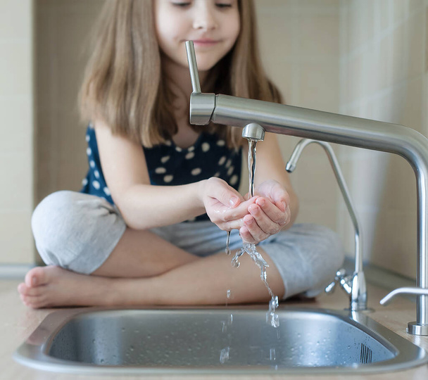 Child open water tap. Kitchen faucet. Glass of clean water. Pouring fresh drink. Hydration. Healthy lifestyle. Water quality check concept. World water monitoring day. Environmental pollution problem - Фото, изображение