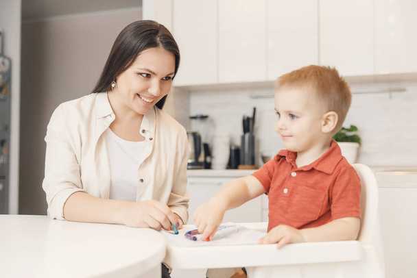 Äiti opettaa poikaansa piirtämään lyijykynillä paperille valkoinen keittiö tausta
 - Valokuva, kuva