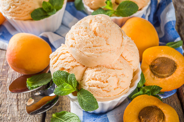 Homemade sweet apricot ice cream. Apricot gelato balls in small bowls, on wooden background with fresh apricots and mint leaves - Photo, Image