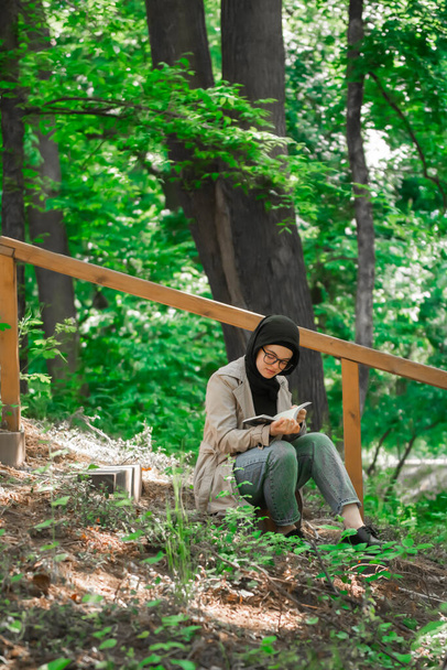 Egy muszlim nő könyvet olvas a parkban a szabadidejében.. - Fotó, kép
