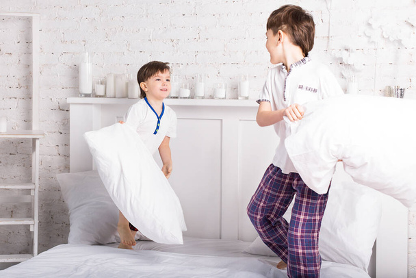 Dwóch braci chłopców, rodzeństwo w piżamie walczące na poduszki w łóżku - Zdjęcie, obraz