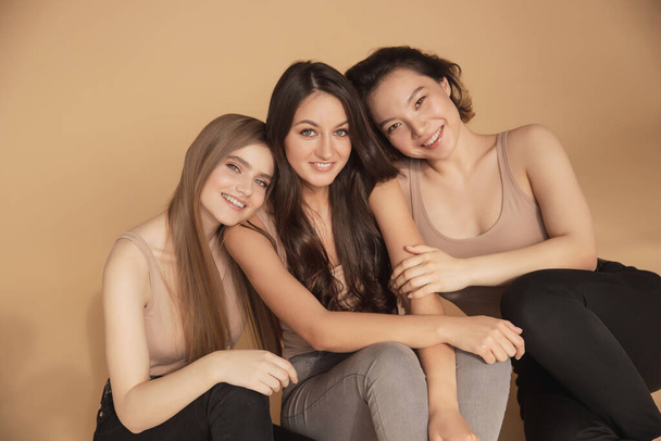 Boldog fiatal multikulturális ázsiai nők, kaukázusi ölelés és nevetés a stúdióban bézs háttérrel. Szépségfürdő kezelés bőrápolási koncepció - Fotó, kép