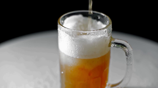 powolny ruch zimnego piwa wlewającego się do kubka na białej powierzchni odizolowanej na czarno - Materiał filmowy, wideo
