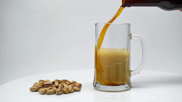 slow motion of dark beer pouring into mug near pistachios isolated on white - Filmmaterial, Video