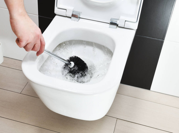 A male hand cleans the toilet with a brush. - Zdjęcie, obraz