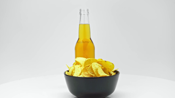 üveg világos sör és chips fekete tálban forgó asztalon elszigetelt fehér - Felvétel, videó