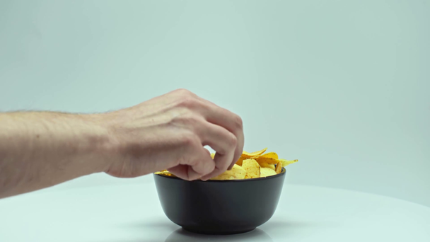 cropped view of man taking crispy chips from black bowl isolated on white - Filmati, video