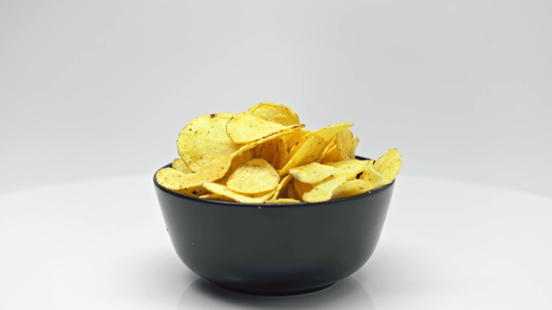 black bowl full of crispy chips rotating on white surface isolated on white - Footage, Video