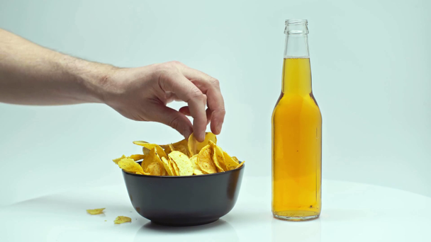 bijgesneden beeld van de mens het nemen van chips en fles licht bier geïsoleerd op wit - Video