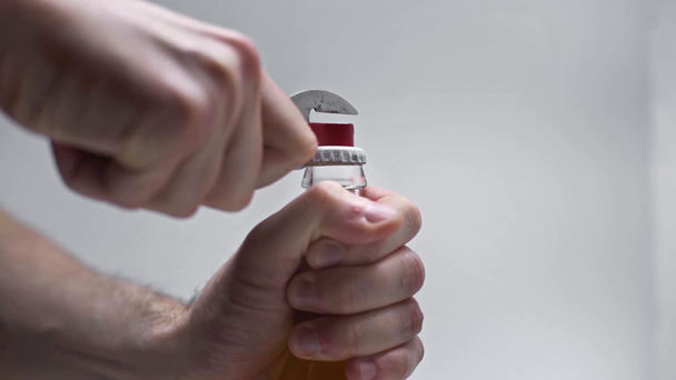 abgeschnittene Ansicht eines Mannes, der eine Flasche Bier mit Dosenöffner auf grauem Hintergrund öffnet - Filmmaterial, Video