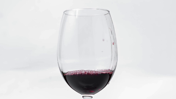 Αργή κίνηση του κόκκινου κρασιού χύνοντας σε ποτήρι σε λευκό  - Πλάνα, βίντεο