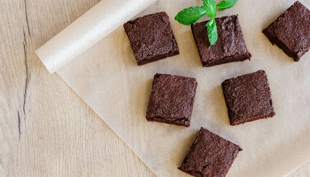 Freshly baked classic fudge brownie on parchment brown paper and wooden table background. Homemade sweet food.  - Фото, зображення