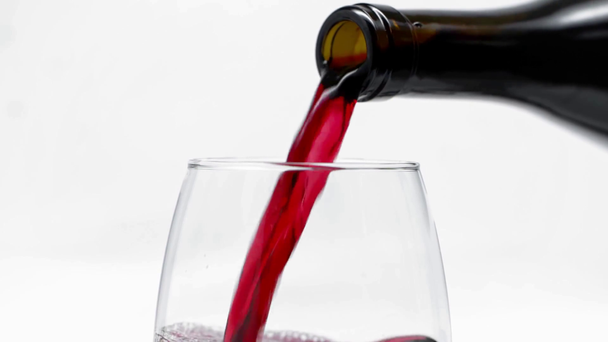 Langzame beweging van rode wijn gieten in glas uit fles op wit  - Video