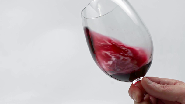 Powolny ruch człowieka wirujący kieliszek czerwonego wina wyizolowanego na białym  - Materiał filmowy, wideo