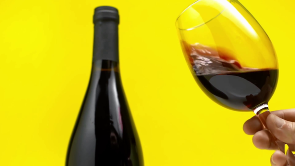 Pomalý pohyb člověka vířící sklo červeného vína izolované na žluté  - Záběry, video