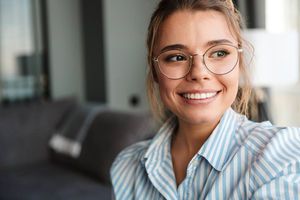 Image closeup of cheerful nice woman wearing eyeglasses smiling and looking aside in bright room - Фото, изображение
