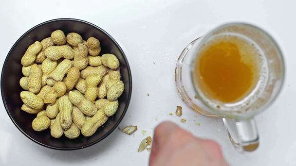cropped view of man eating peanuts and drinking light beer on white table - Footage, Video