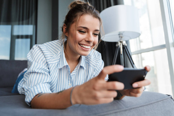 Happy young businesswoman using mobile phone while relaxing on a couch at home - Zdjęcie, obraz
