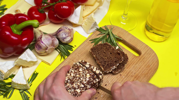 καλλιεργημένη άποψη του ανθρώπου κοπής ψωμί σίκαλης κοντά σε μπουκάλι κρασί  - Πλάνα, βίντεο