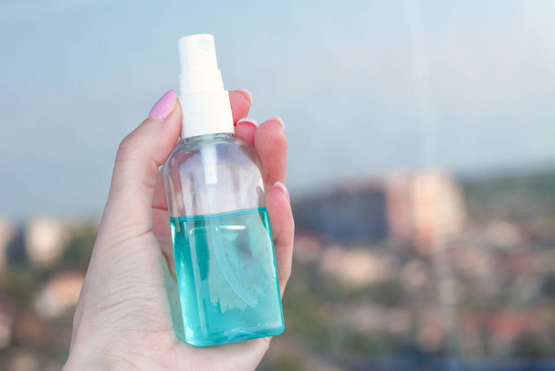 女の子の手のガラス瓶に手のための1つの青い防腐剤。窓には都市が反映されている。コヴィト19世からの都市と人々の保護の概念 - 写真・画像