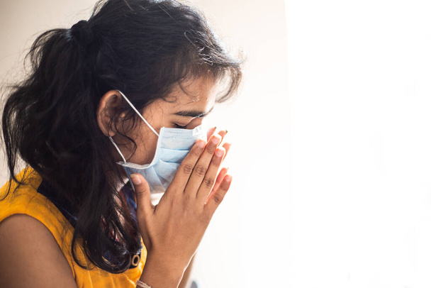 COVID-19コロナウイルスの肖像画保護マスクのくしゃみをしている若いアジア系インド人の少女。コヴィッド19からの保護は白地に隔離されてる。熱、風邪、インフルエンザを患っている女の子. - 写真・画像
