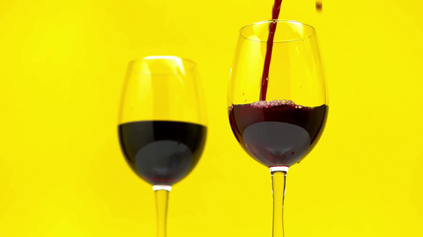 Αργή κίνηση του κόκκινου κρασιού χύνοντας σε ποτήρι που απομονώνονται σε κίτρινο  - Πλάνα, βίντεο