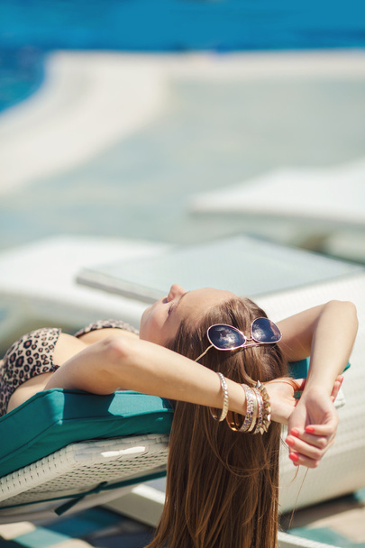 Woman sunbathing in bikini at tropical travel resort. Beautiful young woman lying on sun lounger near pool - 写真・画像