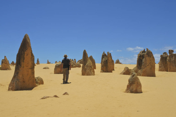 Австралиец, путешествующий по дикой местности с видом на вершины пустыни близ Перта в Западной Австралии. Пустыня содержит тысячи известняковых образований, называемых вершины
 - Фото, изображение