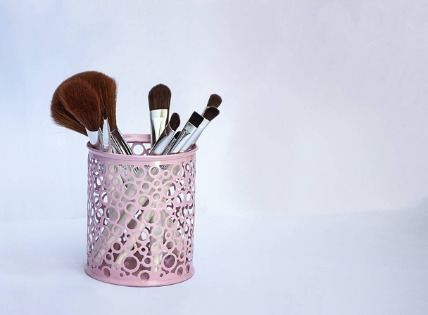 Set de pinceles de maquillaje en un vaso de hierro rosa sobre un fondo claro
 - Foto, Imagen
