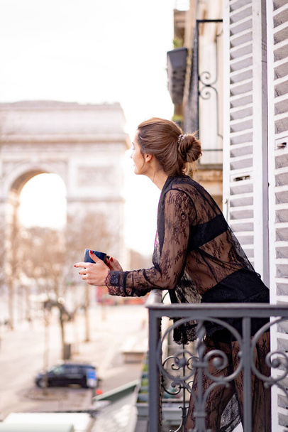 Attractive yang woman in pajama is drinking coffee on balcony  - Foto, imagen