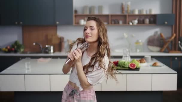 Smiling woman singing song in whisker in kitchen. Cheerful girl having fun - Filmagem, Vídeo