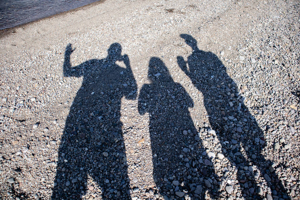 ワイオミング州のイエローストーン湖のビーチでスマートフォンで影の写真を撮る3人 - 写真・画像