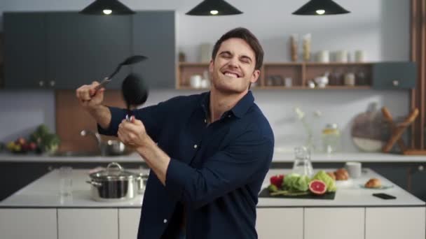 Cheerful man having fun at home kitchen. Energetic guy drumming with utensil - Felvétel, videó