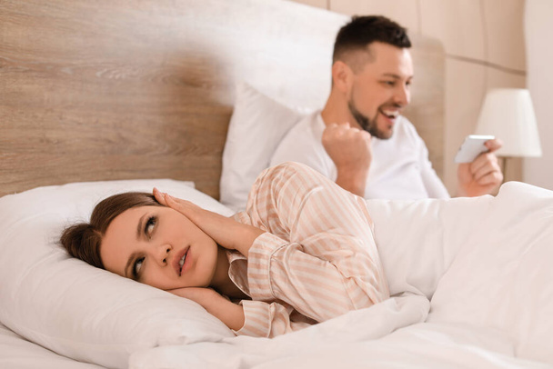 Young woman cannot sleep because of her husband playing game on mobile phone in bedroom - Φωτογραφία, εικόνα