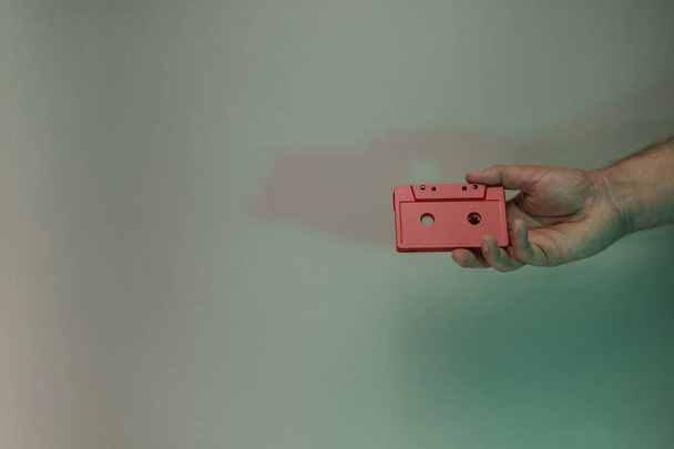 Hand holding red audio cassette tape in the color light. Beautiful minimal in neon light. Minimalism retro style concept. Background pattern for design.  - Fotografie, Obrázek