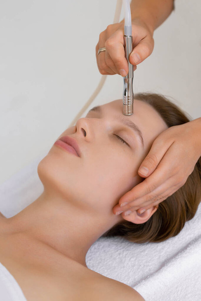 The cosmetologist makes the procedure Microdermabrasion of the facial skin of a beautiful, young woman in a beauty salon.Cosmetology and professional skin care. - Φωτογραφία, εικόνα