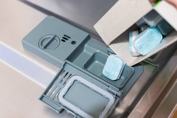 Mies täyttää ekotablettien pesuaineen astianpesukoneessa. Kertakäyttöiset muovitabletit, jotka liukenevat
. - Valokuva, kuva