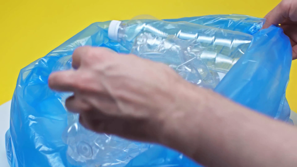 cropped view of man putting plastic bottles in garbage bag isolated on yellow  - Footage, Video