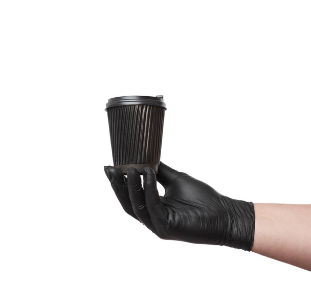 ブラックラテックス手袋の手には使い捨ての段ボールカップとプラスチック製の蓋が白い背景にあり流行時のオンライン注文の安全かつ非接触配信 - 写真・画像