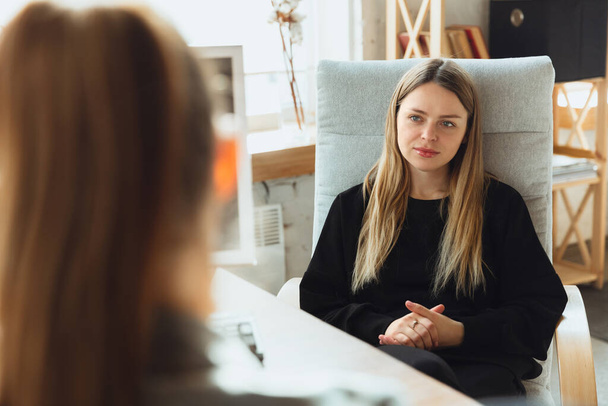 Young woman sitting in office during the job interview with female employee, boss or HR-manager, talking, thinking, looks confident - Fotoğraf, Görsel