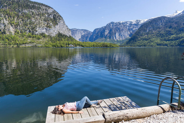 relaxed woman lying on a wooden jetty watching the calm lake reflecting the mountains in austrian tyrol - Photo, Image