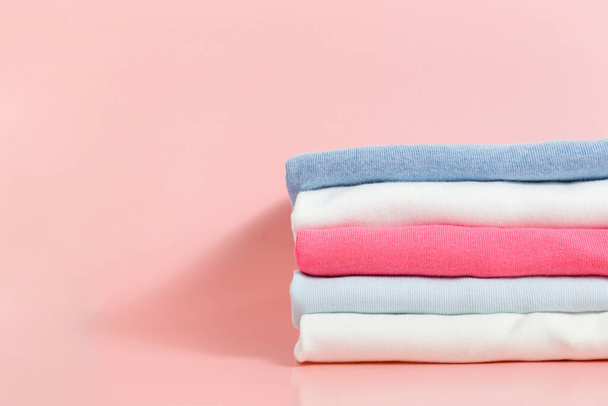 Stack of colorful perfectly folded clothing items. Pile of different pastel color shirts and sweaters isolated on pale pink background. Close up, top view, copy space. - Fotografie, Obrázek