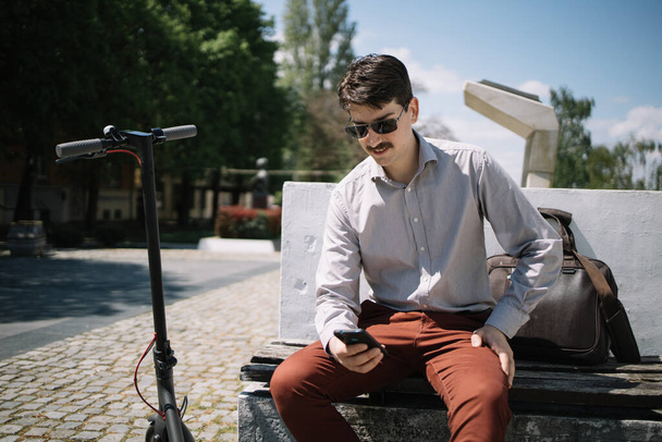 Happy man using phone while sitting on a bench in city - Φωτογραφία, εικόνα