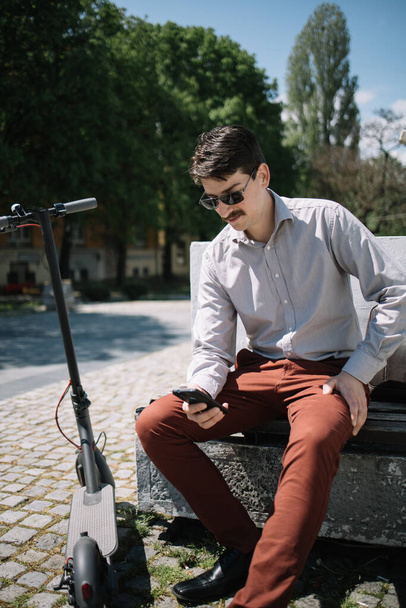 Portrait of a man resting on a bench near electric electric scooter - Fotoğraf, Görsel