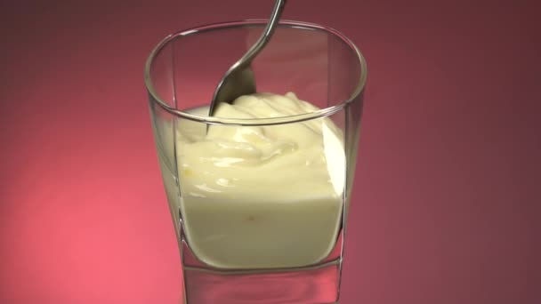 Deja de moverte vertiendo un vaso de yogur vegetariano fresco. Revuelve el yogur con una cuchara. Leche ecológica en un vaso transparente sobre fondo blanco, aislada. Fondo espejo rojo
 - Metraje, vídeo