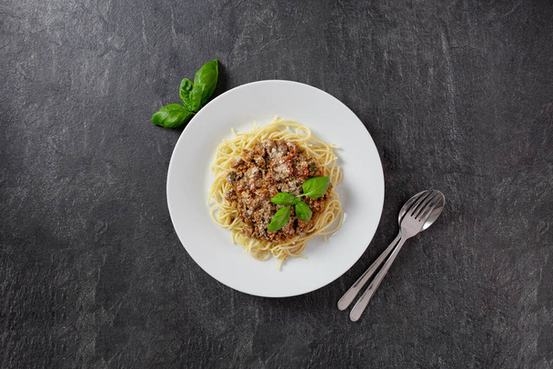 Traditional italian spaghetti Bolognese with meat and tomato sauce in a plate. Parmesan cheese, fresh tomatoes, basil, spices and herbs. Dark background. Top view. Copy space. - Photo, Image