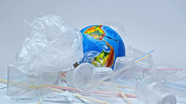 plastic cups falling on globe near trash on white - Imágenes, Vídeo