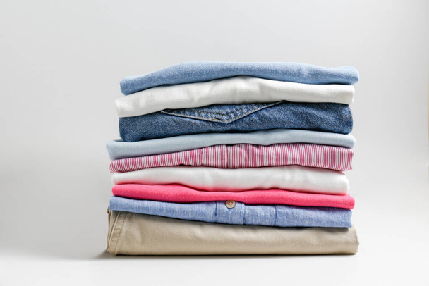 Stack of colorful perfectly folded clothing items. Pile of different pastel color shirts, sweaters isolated and other garments on white background. Close up, copy space. - Photo, image